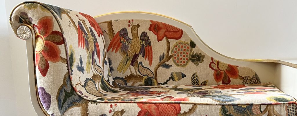 Close-up of a re-upholstered piece of furniture with a multi-colour pattern of flowers and birds on a cream background.
