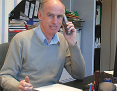 Alan from A.J. Brett is sitting at his desk in his office while speaking on the phone.